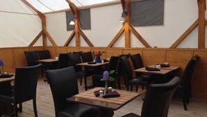 Un restaurante con mesas y sillas de madera, un techo tipo tienda y un diseño interior sencillo.