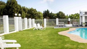 Ein modernes Haus mit Schwimmbad, umzäunter Garten und Gartenmöbeln.