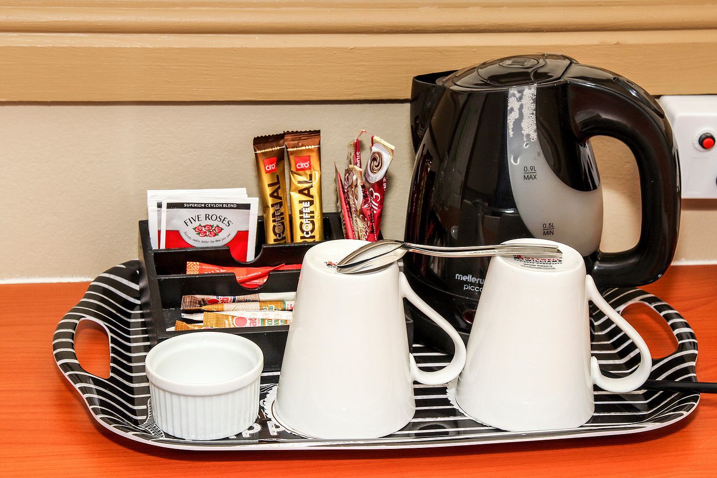 A tray with coffee cups, a kettle, and coffee packets on a wooden table.