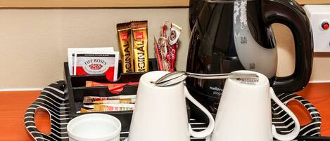 A tray with coffee cups, a kettle, and coffee packets on a wooden table.
