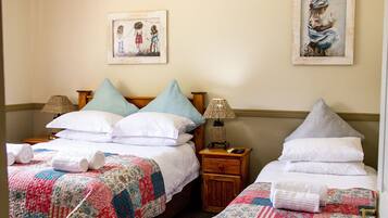 A hotel room with two beds, each with a quilted bedspread, pillows, and a nightstand with a lamp. There are framed pictures on the wall above the beds.