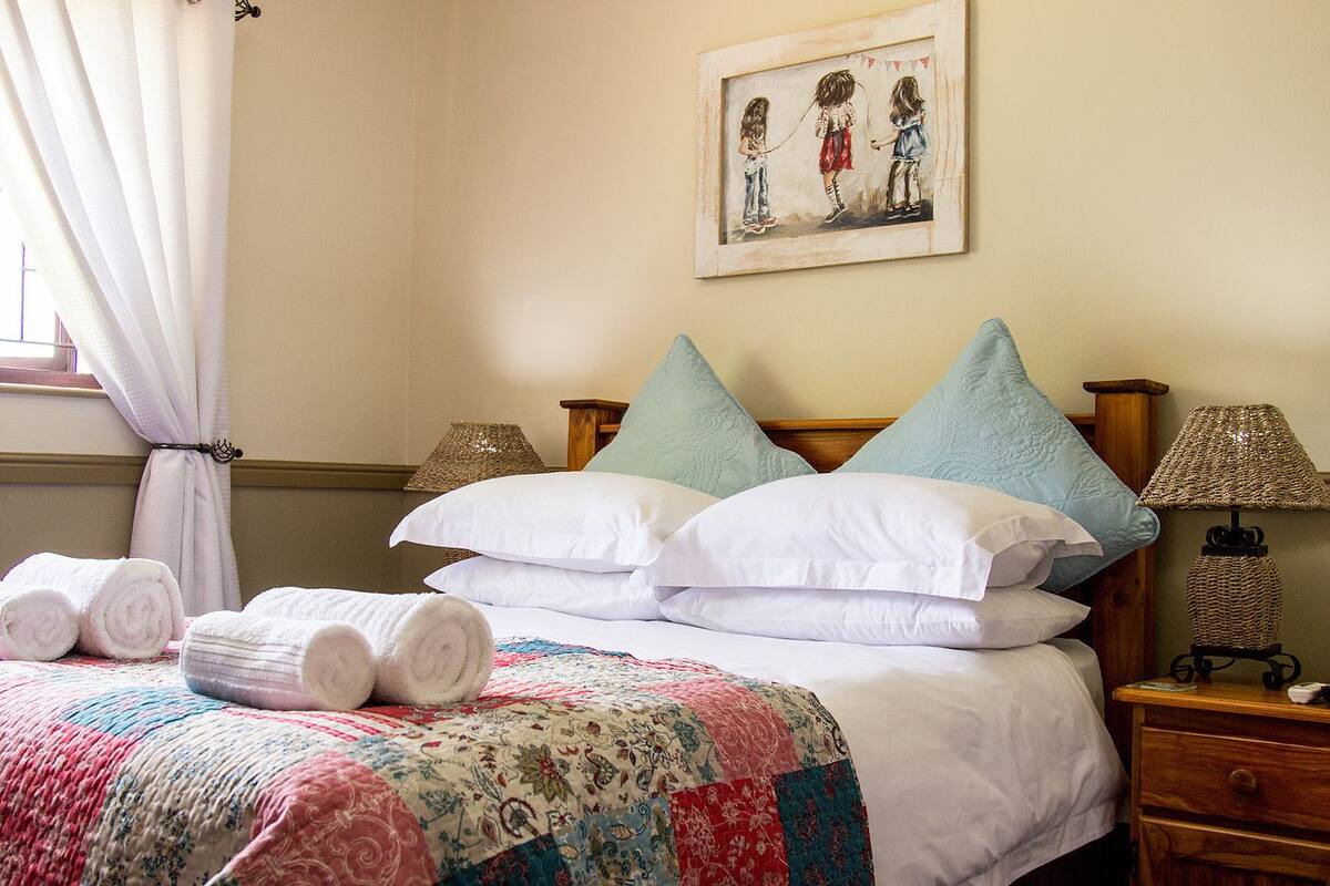 A neatly made bed with rolled towels, a colorful quilt, and decorative pillows.