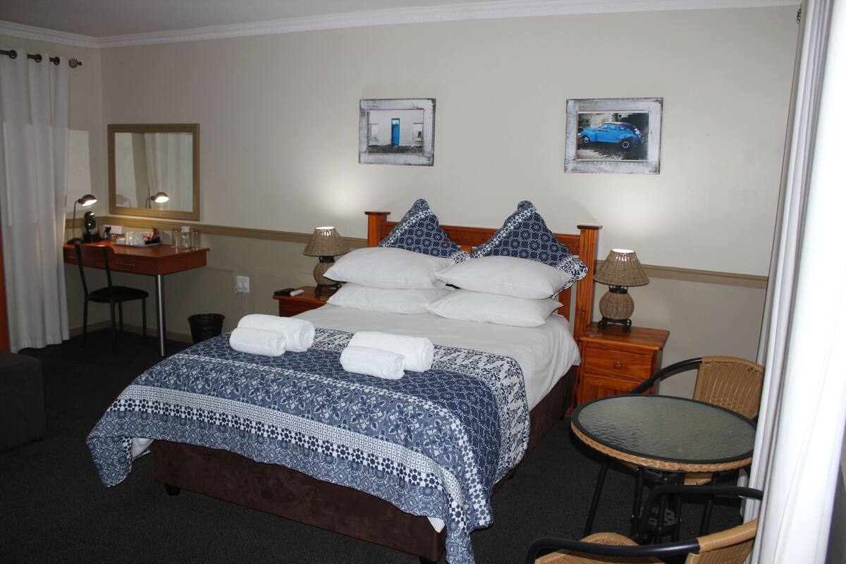 A hotel room with a bed, a desk, a chair, a small table, and two wall-mounted lamps.
