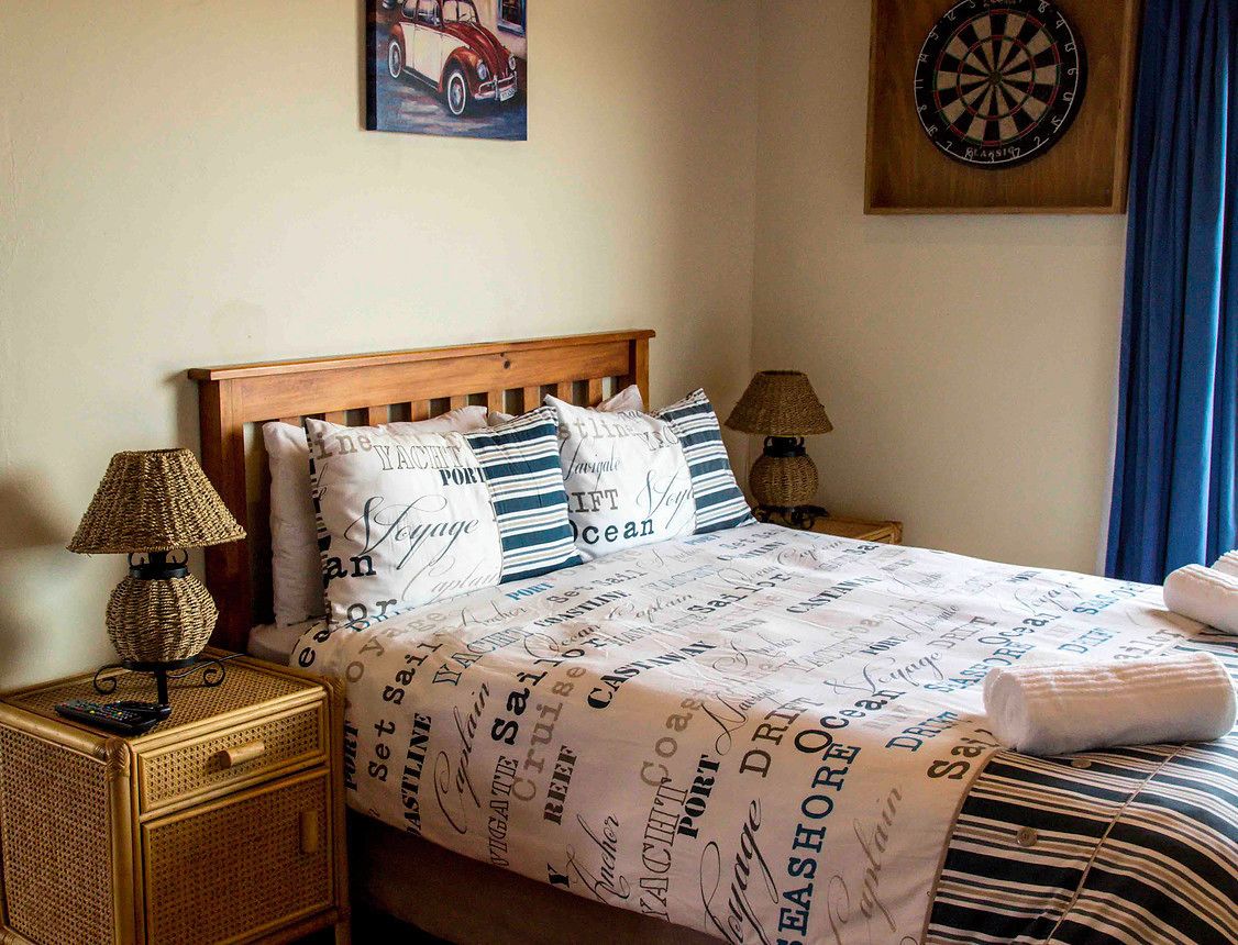 Una cama bien hecha con almohadas a rayas, un cabecero de madera y un dardo en la pared.