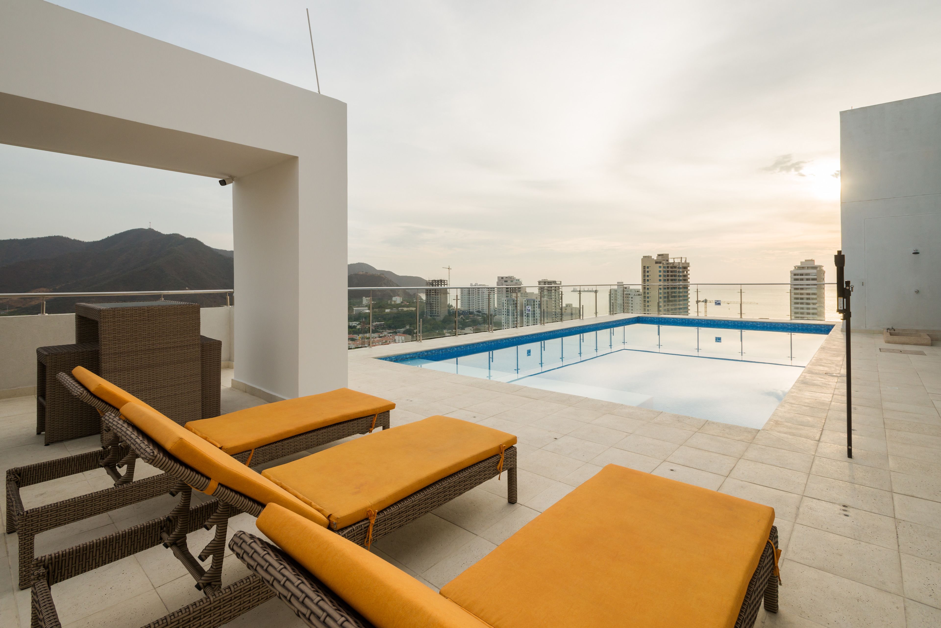 Una terraza en la azotea con piscina, sillones de descanso y vistas a la ciudad y montañas.