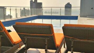 Zona de piscina en la azotea con sillones de mimbre y vistas del horizonte de la ciudad.