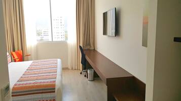 A hotel room with a bed, a desk, a chair, a TV, and a window with curtains.