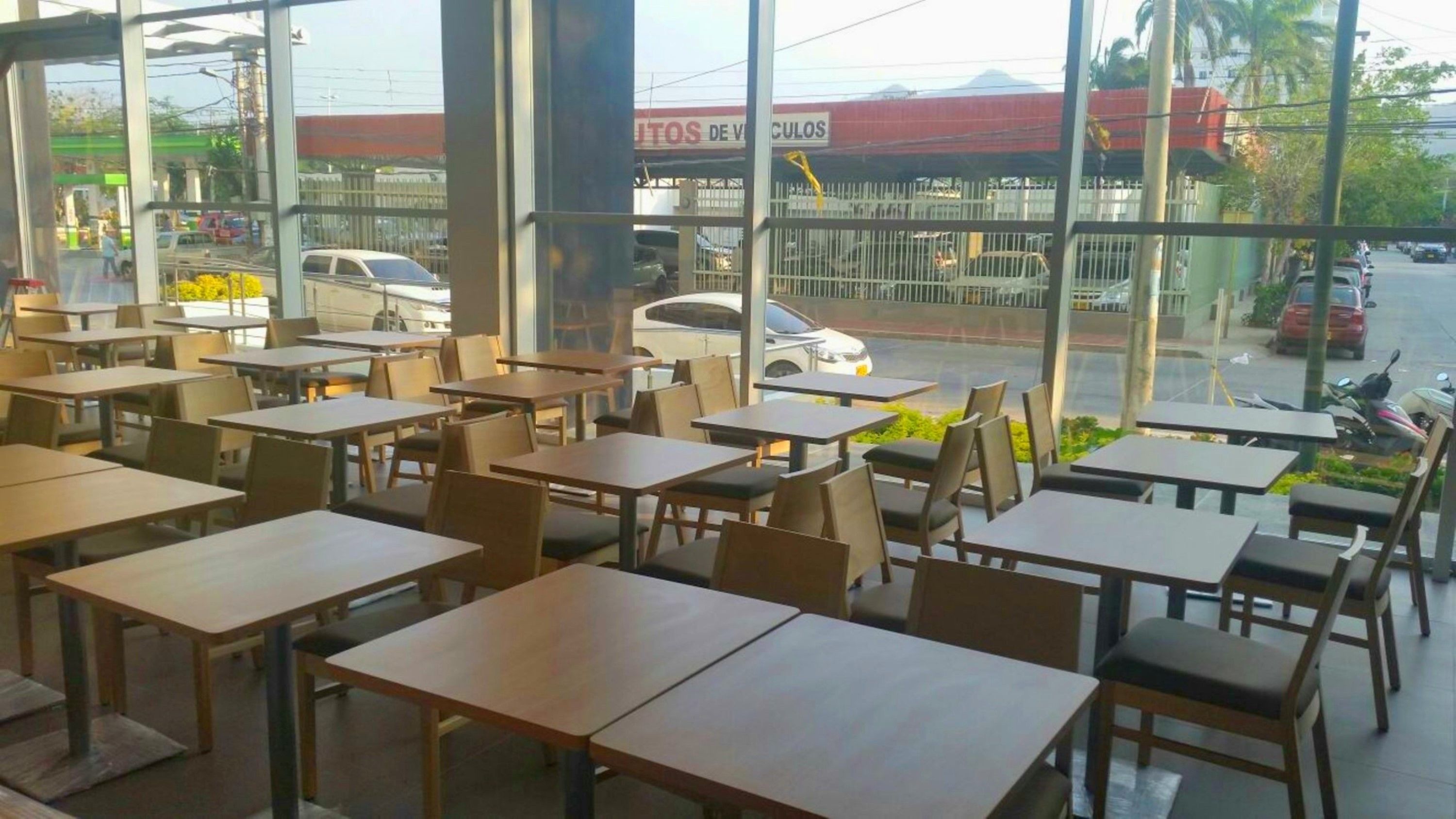 Un restaurant dont l’intérieur est aménagé avec des tables et des chaises, et de grandes fenêtres qui donnent sur la rue.