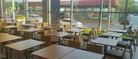 A restaurant with tables and chairs arranged indoors, large windows offering a view of the street outside.