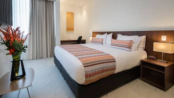 Una habitación de hotel con una cama grande, un escritorio, una silla, una mesita de noche y un jarrón con flores.