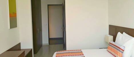 Habitación de hotel con una cama, una mesita de noche, una lámpara y una puerta que da a otra habitación.