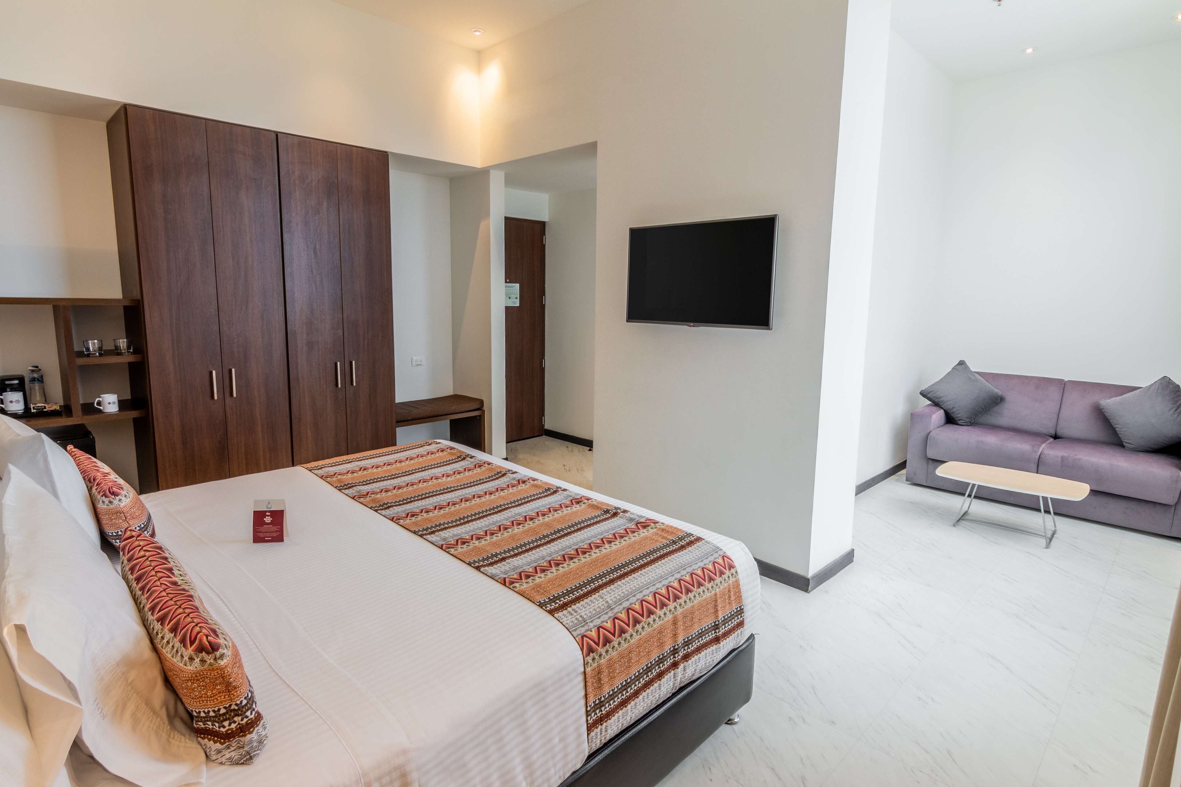 A bedroom with a bed, wardrobe, TV, and a sofa in the adjacent living area.