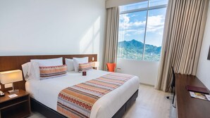 A hotel room with a large bed, a desk, and a view of mountains through the window.