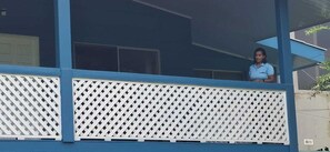 A balcony with a lattice railing, a person standing on it, and a building with large windows in the background. - Cabinas Marielos (Tamarindo)
