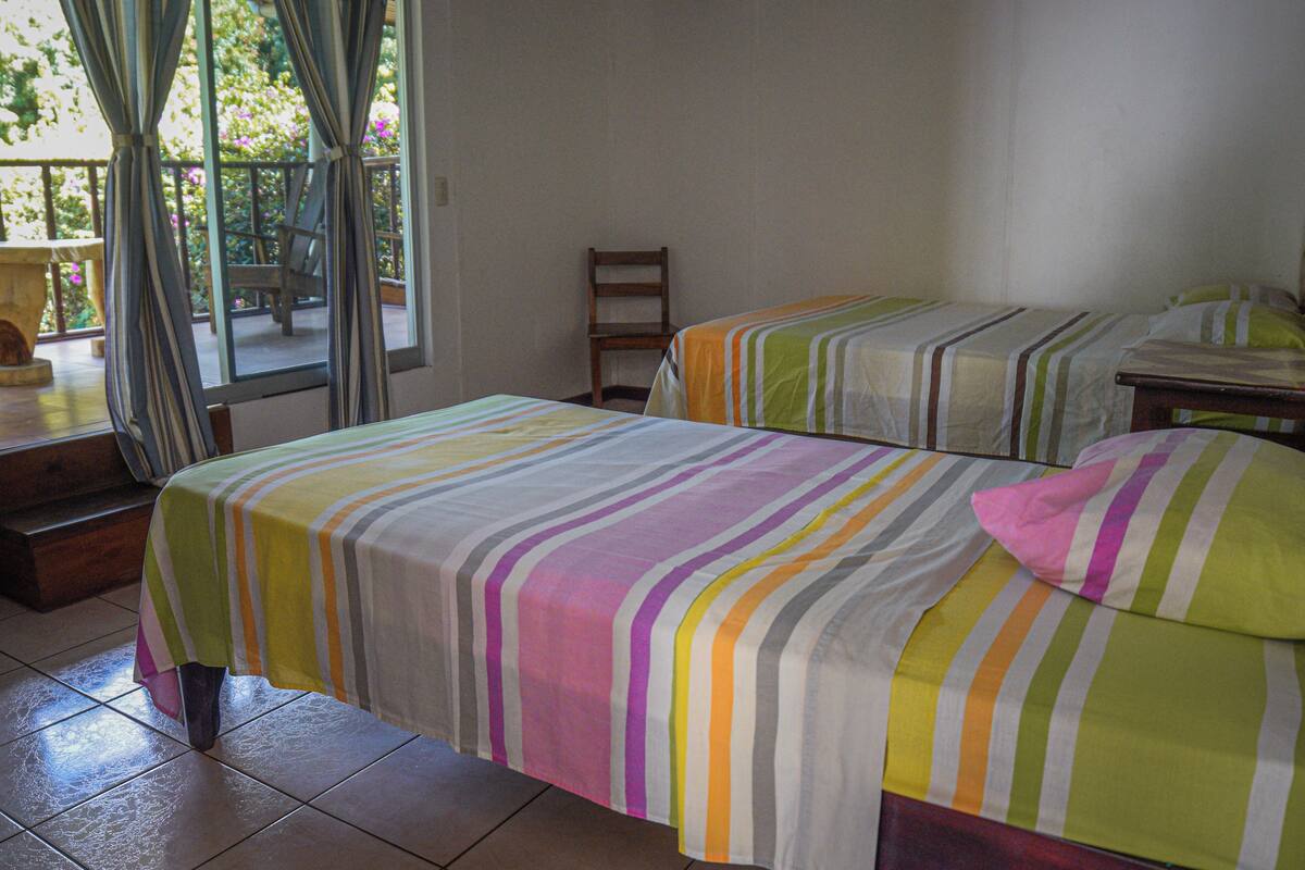 Ein Zimmer mit zwei Betten, einem Sessel und einem fenster mit Vorhängen.