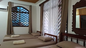 A room with four single beds, a large window with a geometric pattern, and a mirror with an ornate frame. - Cabinas Marielos (Tamarindo)