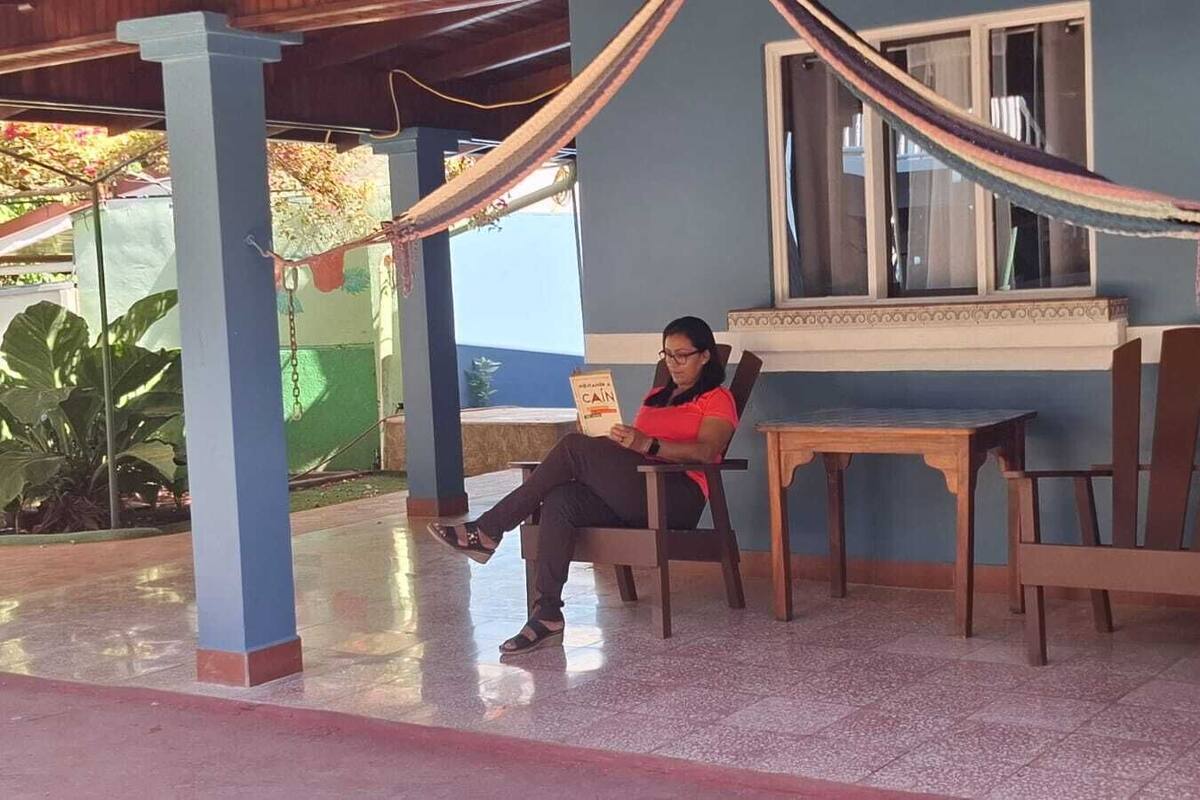 Eine Person sitzt an einem Holztisch mit Stühlen und liest ein Buch.