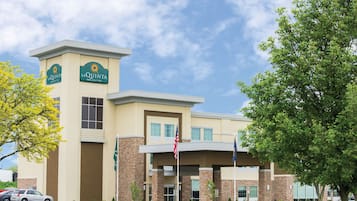 A La Quinta Inn & Suites building with a beige exterior, a flagpole with the American flag, and a clear sky.