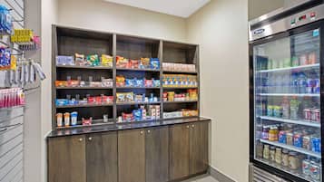 En selvbetjeningsstation med drikkemaskine og hylder fyldt med snacks og drikkevarer.