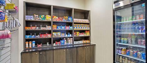 A self-service beverage station with a refrigerated drink dispenser and shelves stocked with snacks and beverages.