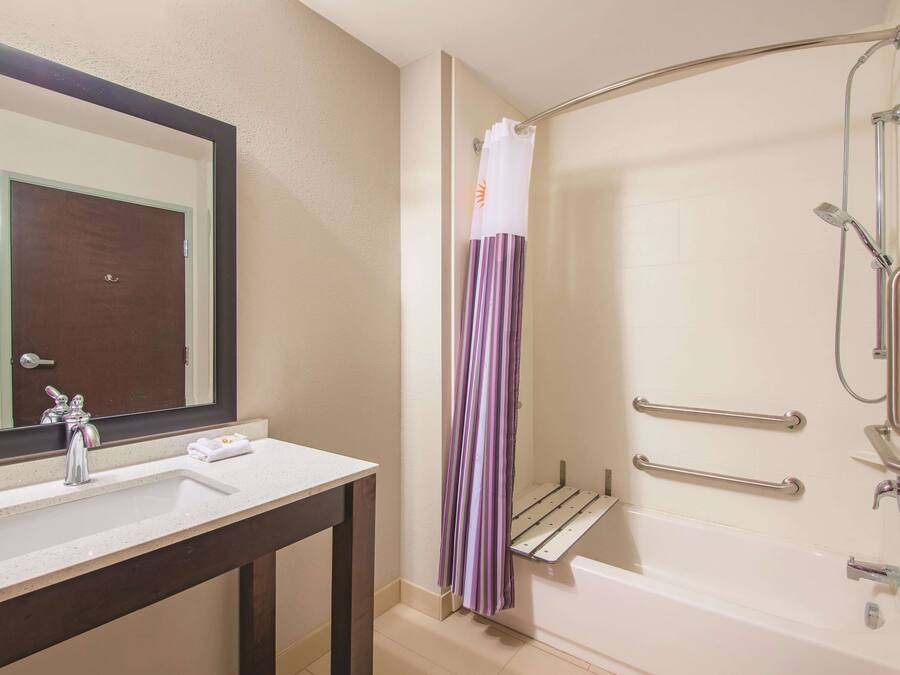 Ein Badezimmer mit Waschbecken, Spiegel, Dusche und Haltestangen.