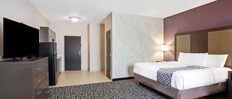 Una habitación de hotel con una cama, un televisor, un aparador y una puerta que da a otra habitación.