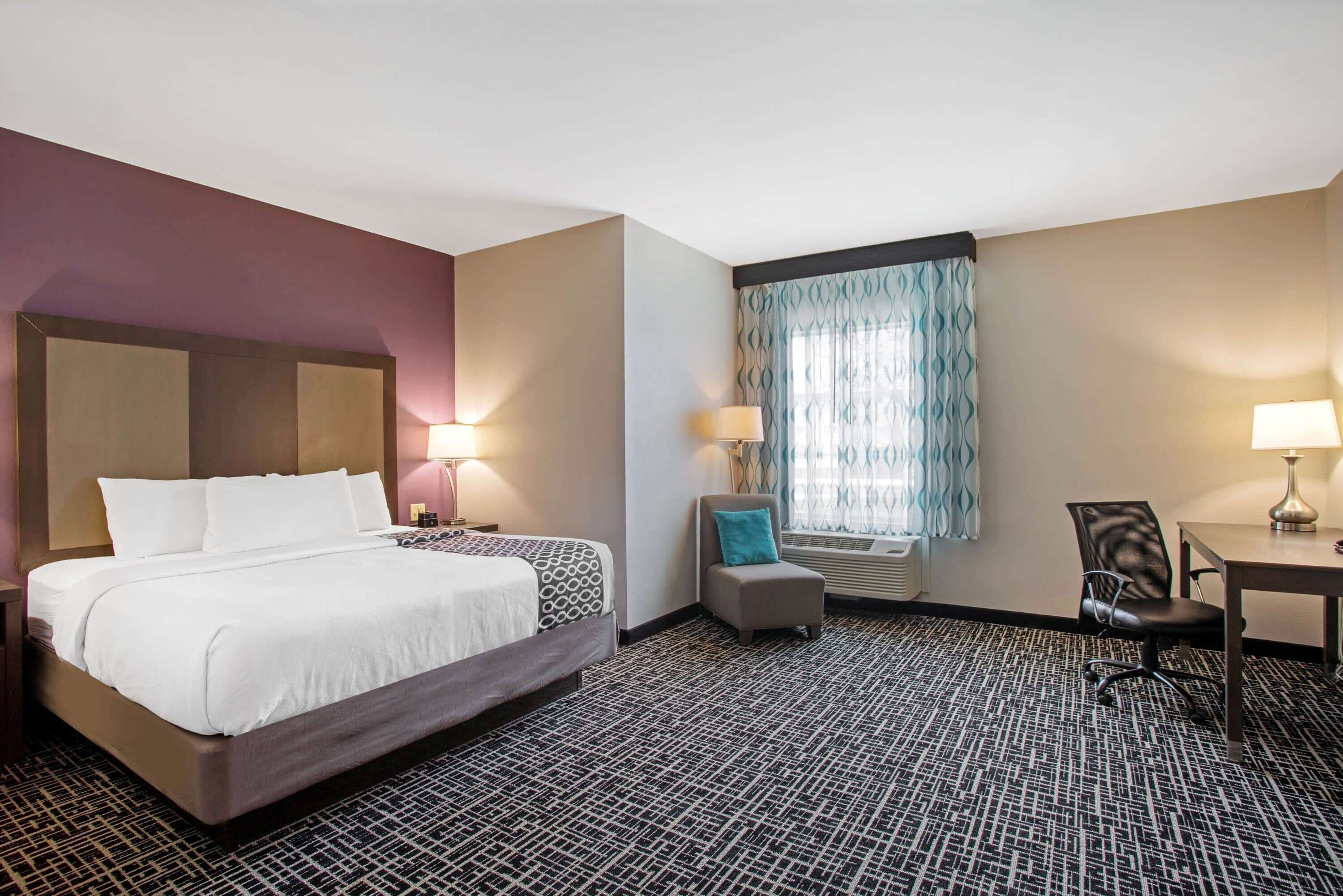 A hotel room with a large bed, a desk, a chair, and a small seating area.
