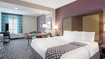 A hotel room with a large bed, a desk, a chair, and a window with patterned curtains.