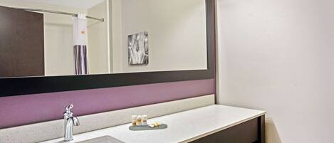 A bathroom with a large mirror, a sink, and a vanity with a countertop.