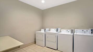A laundry room with four stacked front-loading washers and dryers, a flat folding table, and a tiled floor.