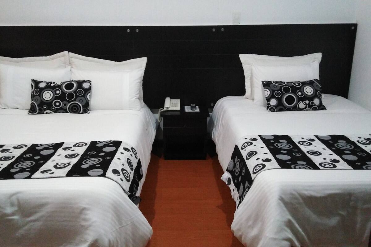Habitación de hotel con dos camas, cada una con una colcha y almohadas a cuadros blanco y negro.