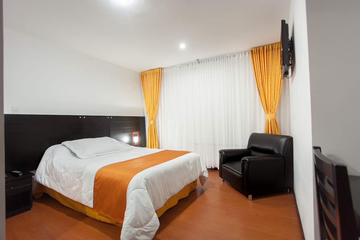 Habitación de hotel con una cama grande, un sillón de cuero negro, un televisor de pantalla plana y una ventana con cortinas.