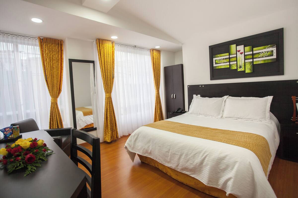 Habitación de hotel con una cama grande, un escritorio con silla, un televisor y un cuadro en la pared.