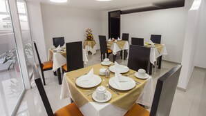 Un espace repas avec des tables dressées pour quatre personnes, chacune agrémentée d’une assiette blanche, de couverts et d’un petit vase de fleurs.