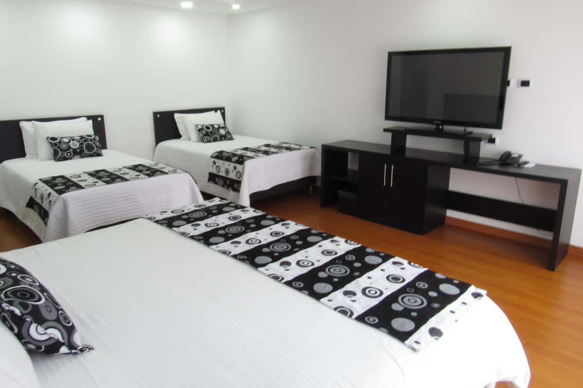 Habitación de hotel con dos camas, televisor y escritorio.