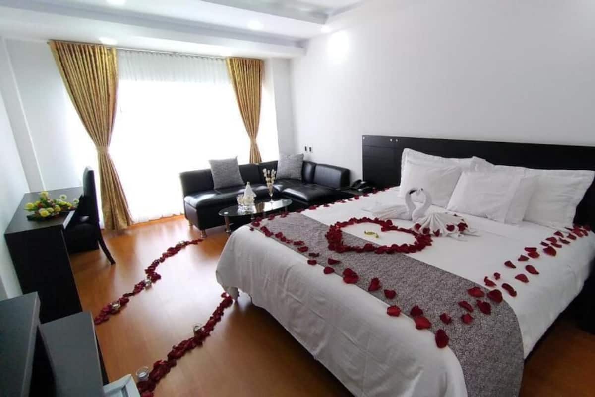 Una habitación de hotel con una cama grande, un escritorio, un sofá y cortinas.