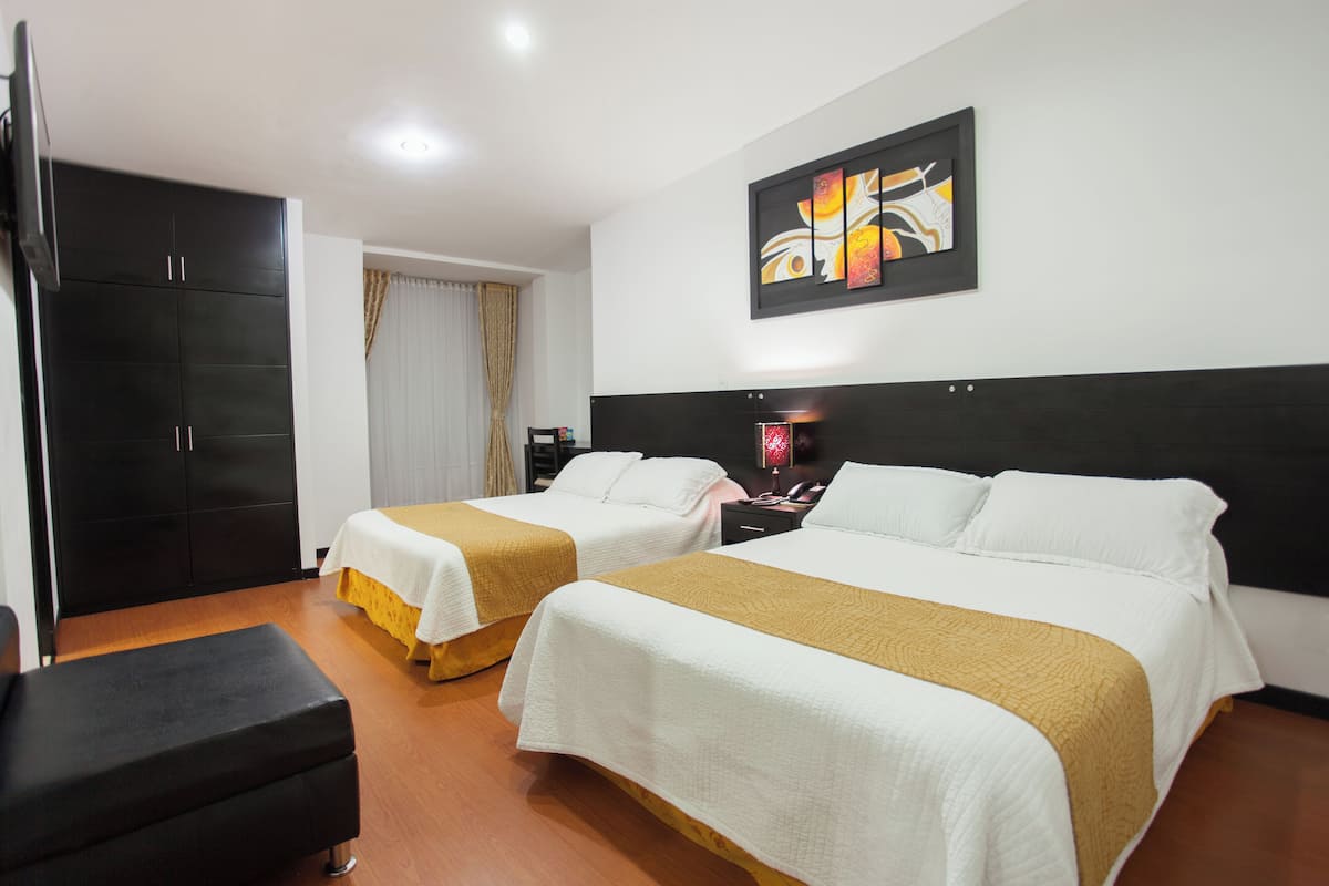 Habitación de hotel con dos camas, un armario, un escritorio y un cuadro en la pared.