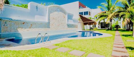 A swimming pool with a stone wall, a thatched-roof structure, and palm trees.