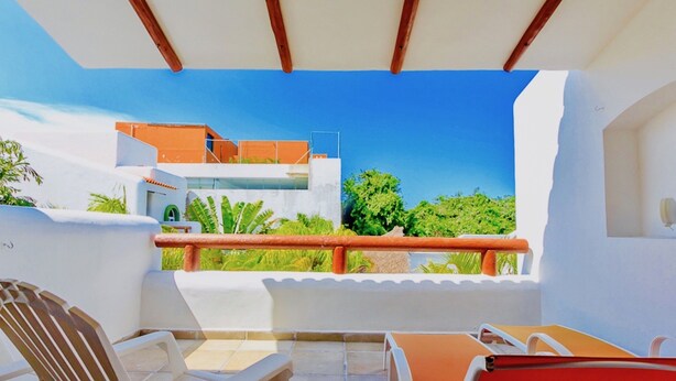 A balcony with a view of a modern building, a table, and two chairs. - Dolce Vita Caribe B&B (Playa del Carmen)