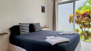 A neatly made bed with striped pillows, a white towel, and a small painting on the wall. - Dolce Vita Caribe B&B (Playa del Carmen)