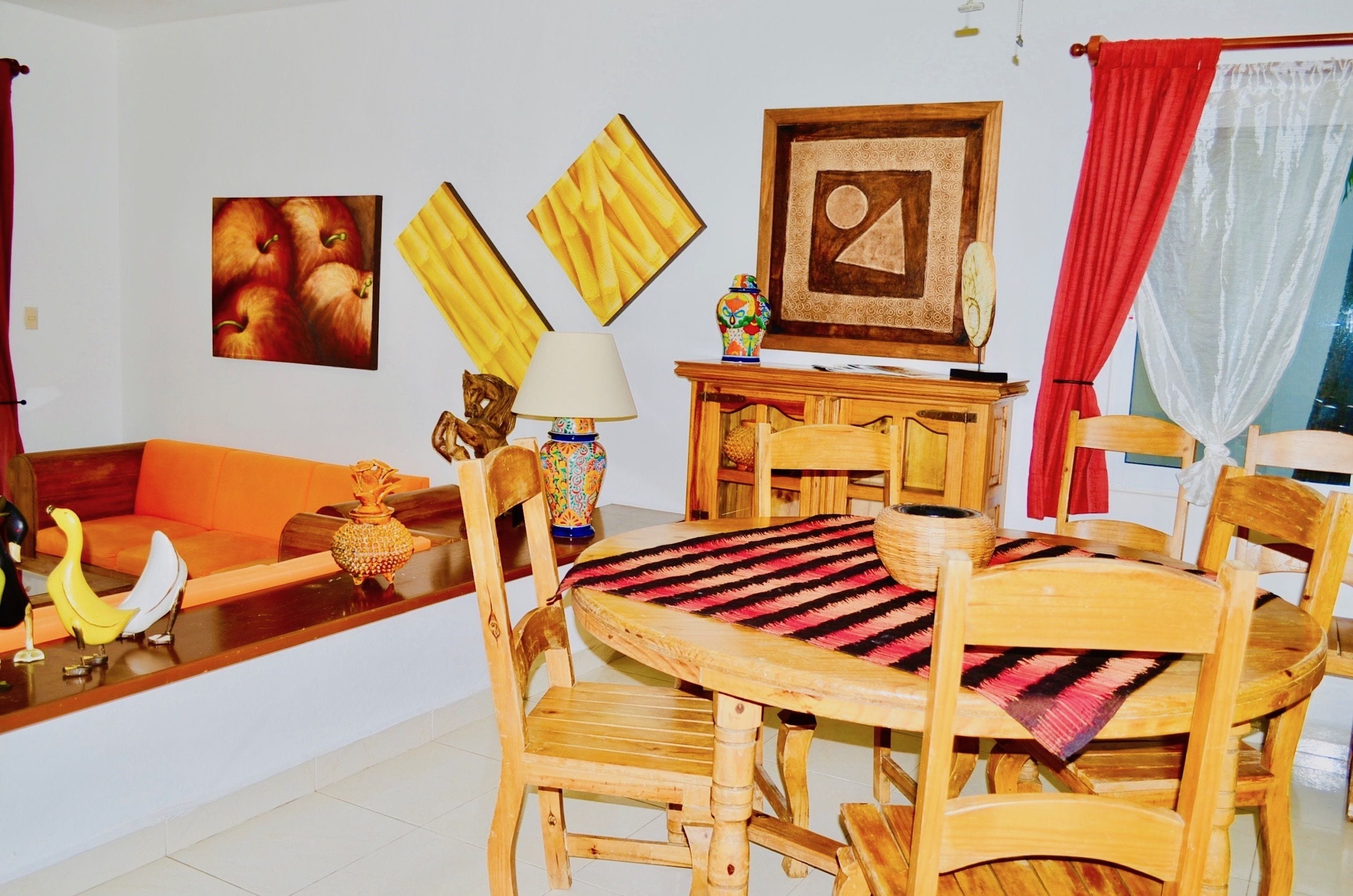 A dining area with wooden furniture, a table with a patterned tablecloth, and wall art including a framed picture and a vase.