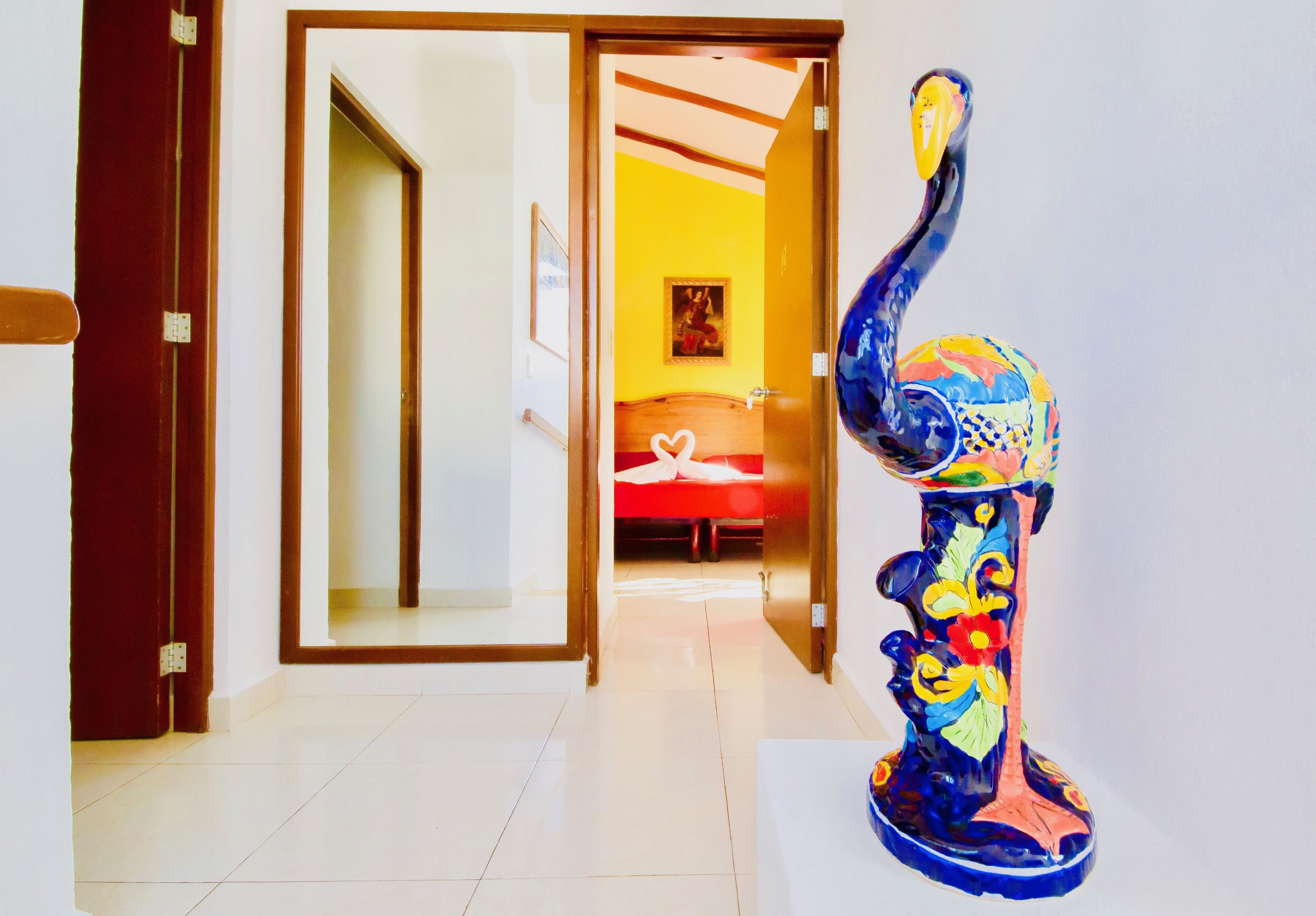 Un couloir avec une grande sculpture colorée sur le côté droit et une porte donnant sur une pièce où se trouve un lit rouge.