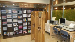 Una librería con estanterías llenas de libros y revistas, un escritorio con ordenador, teclado e impresora, y un cartel en japonés.