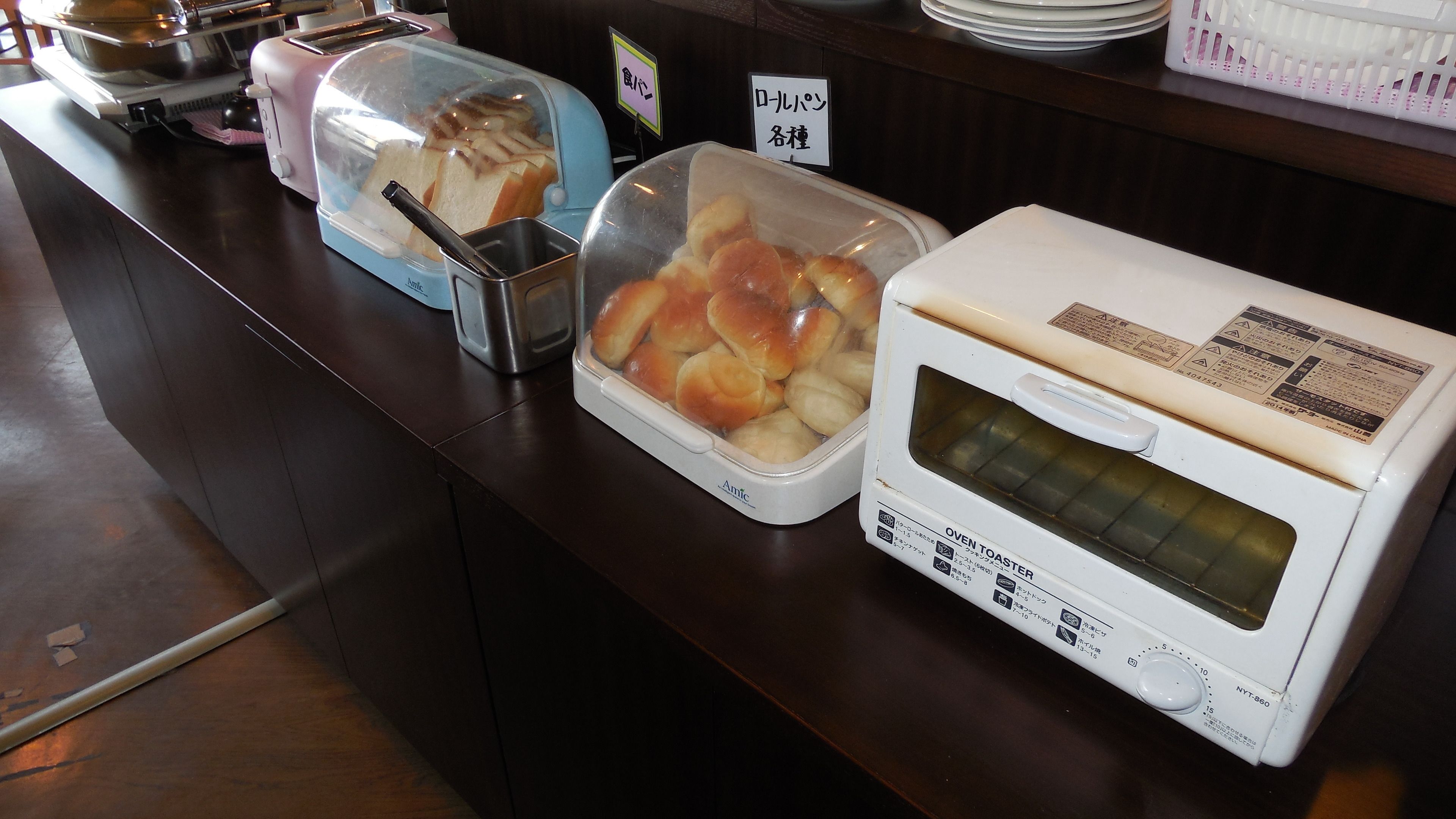 A buffet counter with a toaster oven, a covered container with bread, and a container with rolls.
