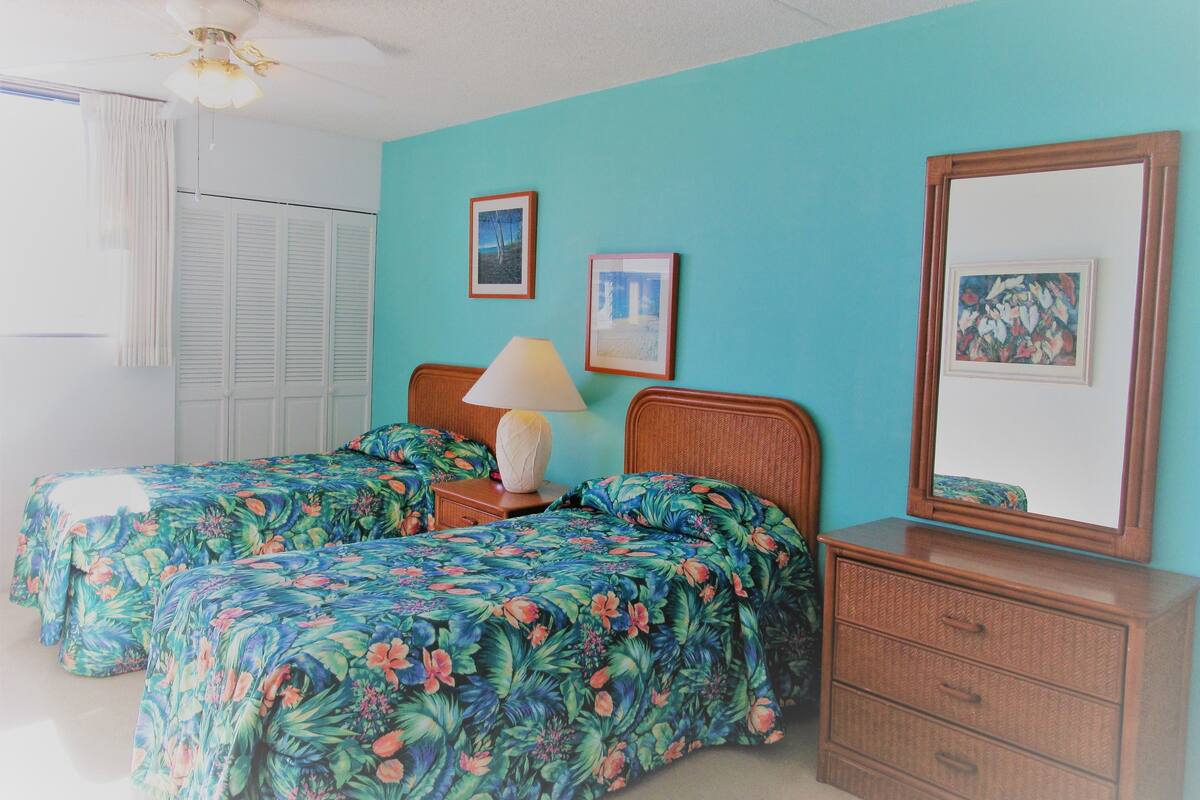 Une chambre avec deux lits, une commode, un miroir et deux tableaux encadrés au mur.