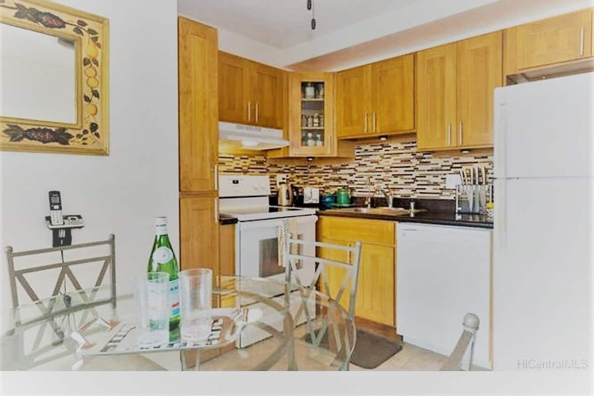 Une cuisine avec des meubles de rangement en bois, un réfrigérateur blanc, une cuisinière et un four à micro-ondes. On y trouve une table à manger avec des chaises et un plateau en verre.