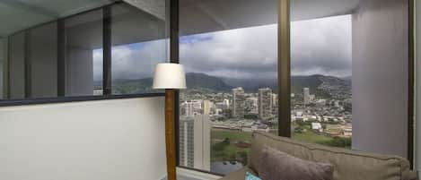 Ein modernes Wohnzimmer mit großem Fenster und Blick auf die Stadt, einer Stehlampe und einem beige-farbenen Sofa mit gemusterten Kissen.
