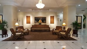 A lobby with a central sofa, two armchairs, a chandelier, and potted plants. - Royal Hawaiian Hospitality (Honolulu)
