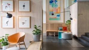 Un interior moderno con una pared de madera, arte con motivos de fauna enmarcados, un banco, una planta y un cartel de elevador para coches.