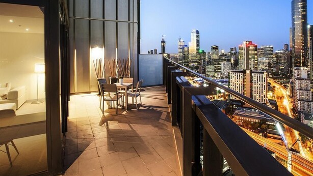 Un balcón moderno con vista a la ciudad, una zona de comedor con sillas y una mesa, y un vidrio que da a una habitación.